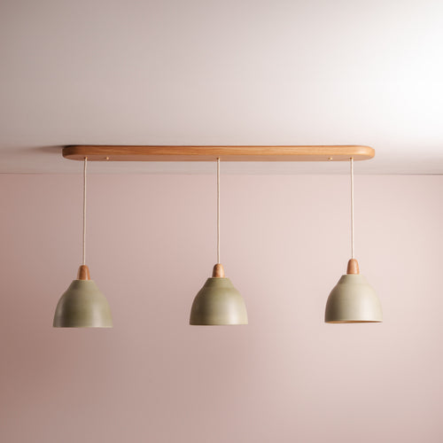 Three ceramic pendant lights with oak wooden fixtures and green ceramic shades on a plain wall.
