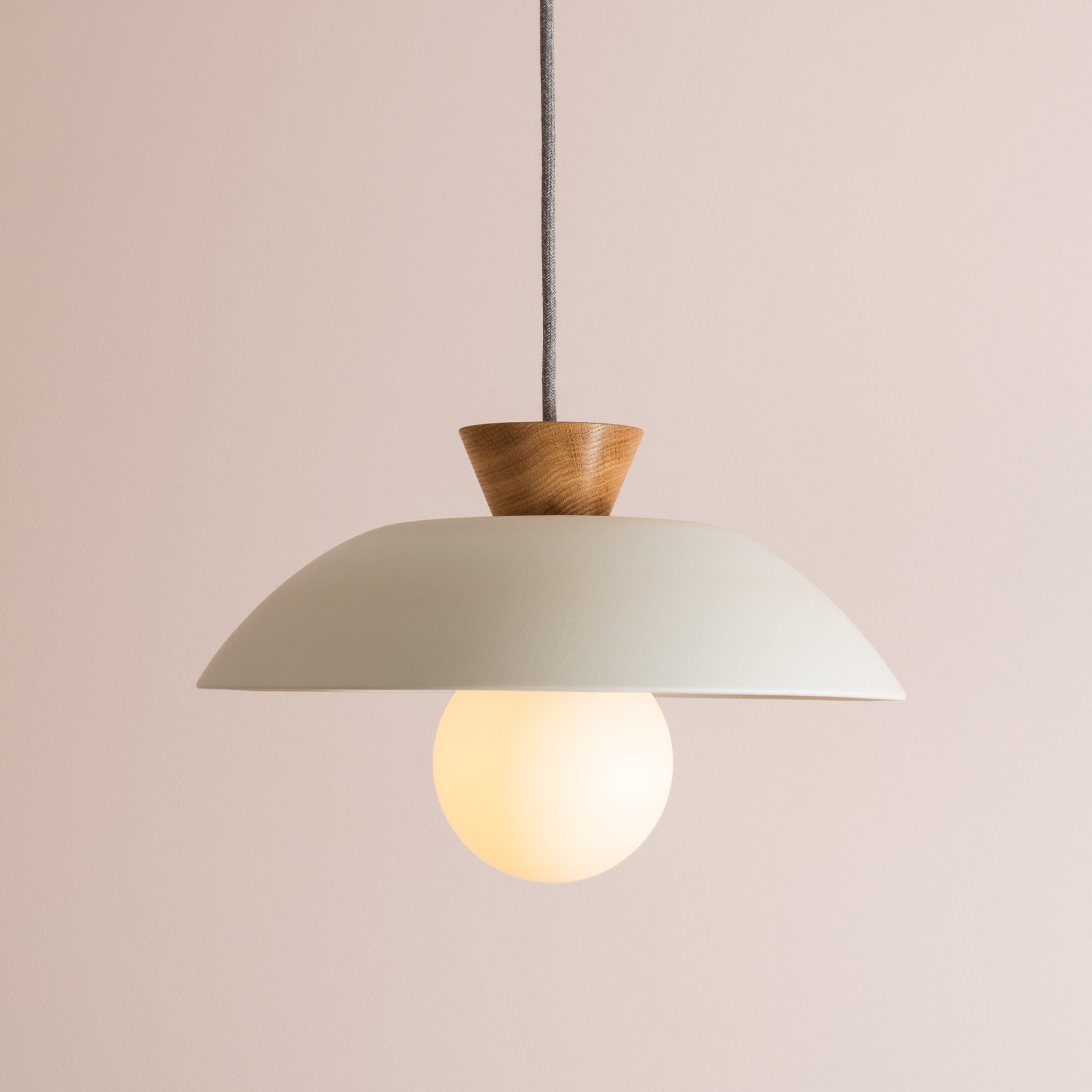 Side view of white ceramic pendant light with round bulb and oak end cap