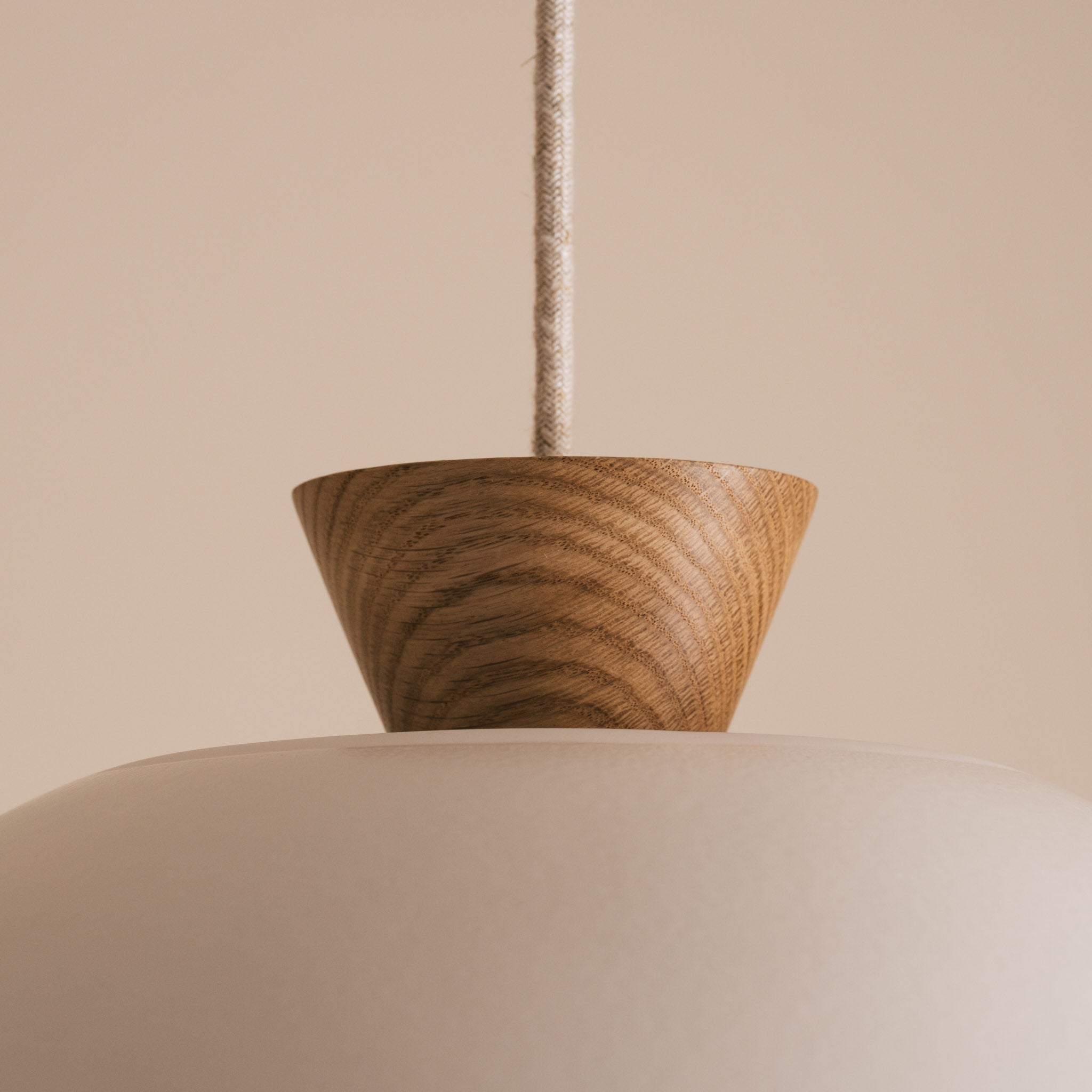 Close-up of oak end cap of ceramic pendant light against a beige background